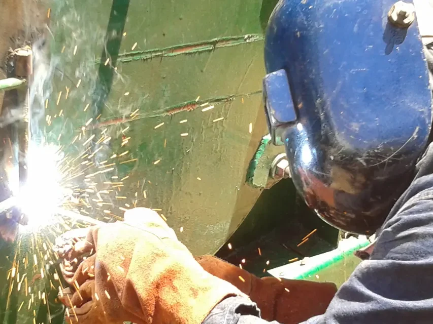 Soldador de Alquiser reparando la lámina de un tanque, con chispas de soldadura