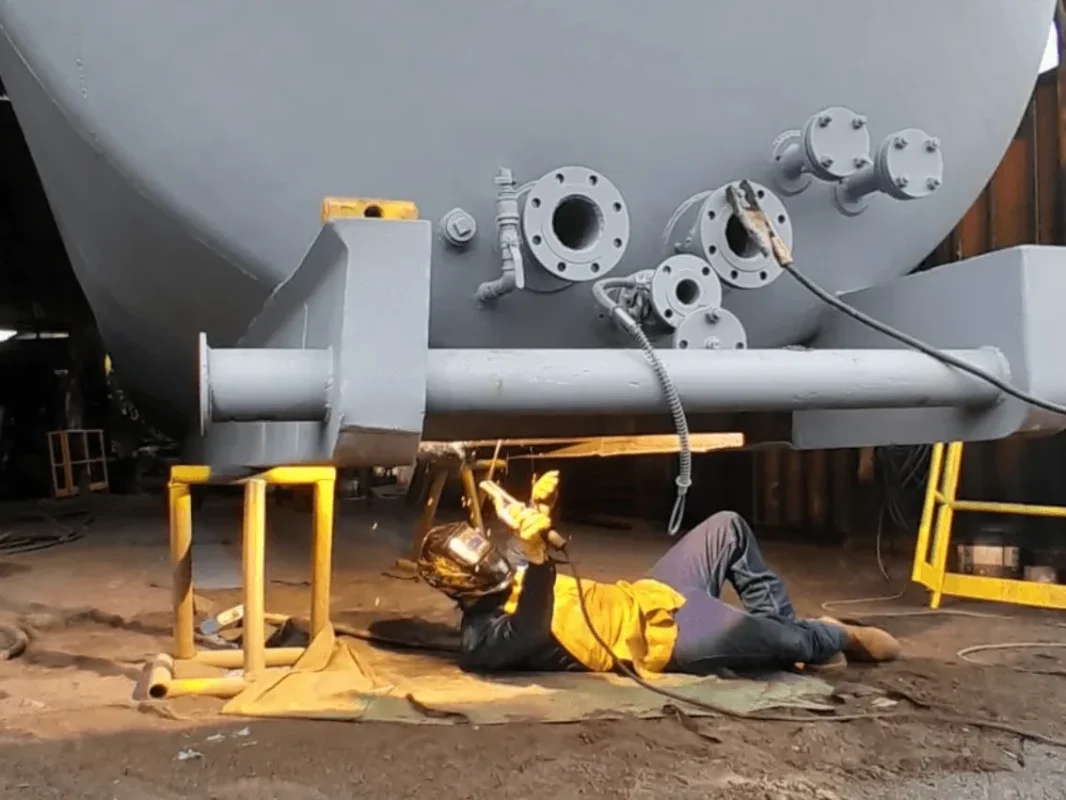 Operario aplicando sandblasting bajo un tanque cilíndrico en el taller de Alquiser